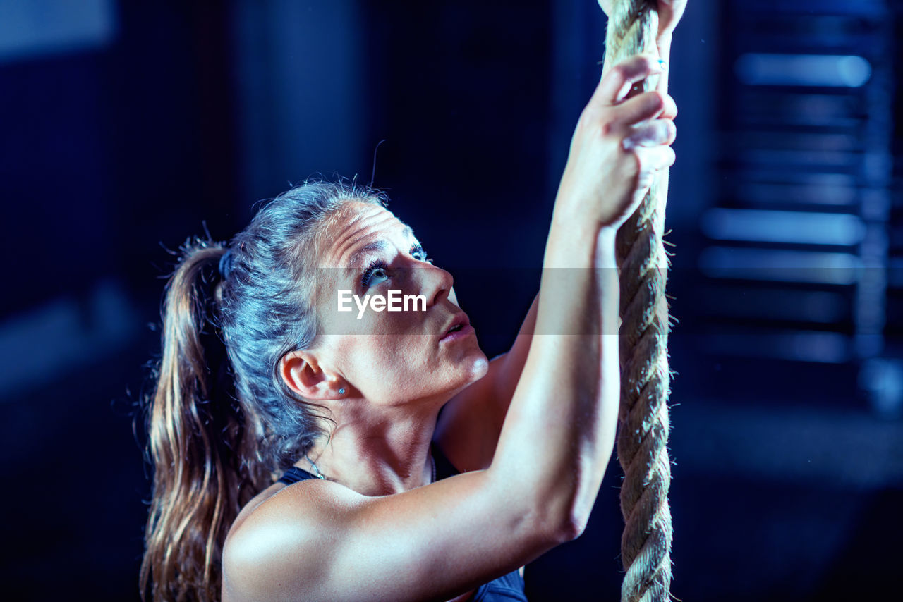 Close-up of female athlete climbing on rope in gym