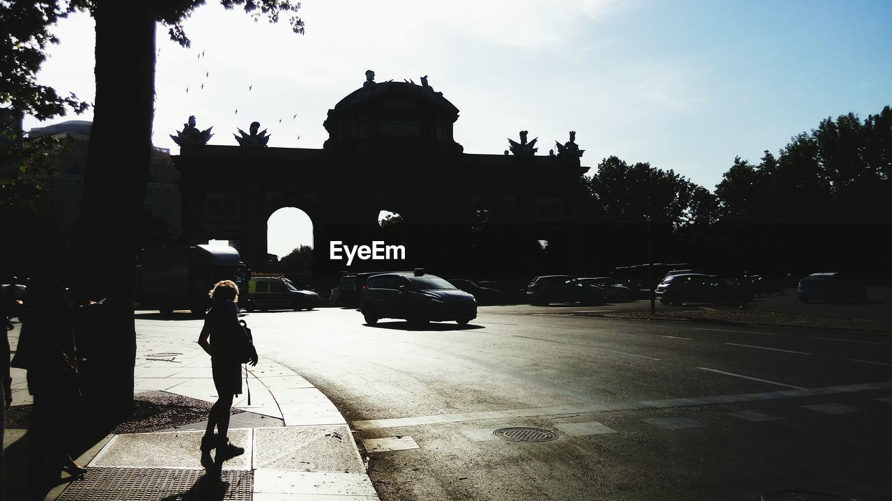 REAR VIEW OF A SILHOUETTE WOMAN WALKING ON ROAD