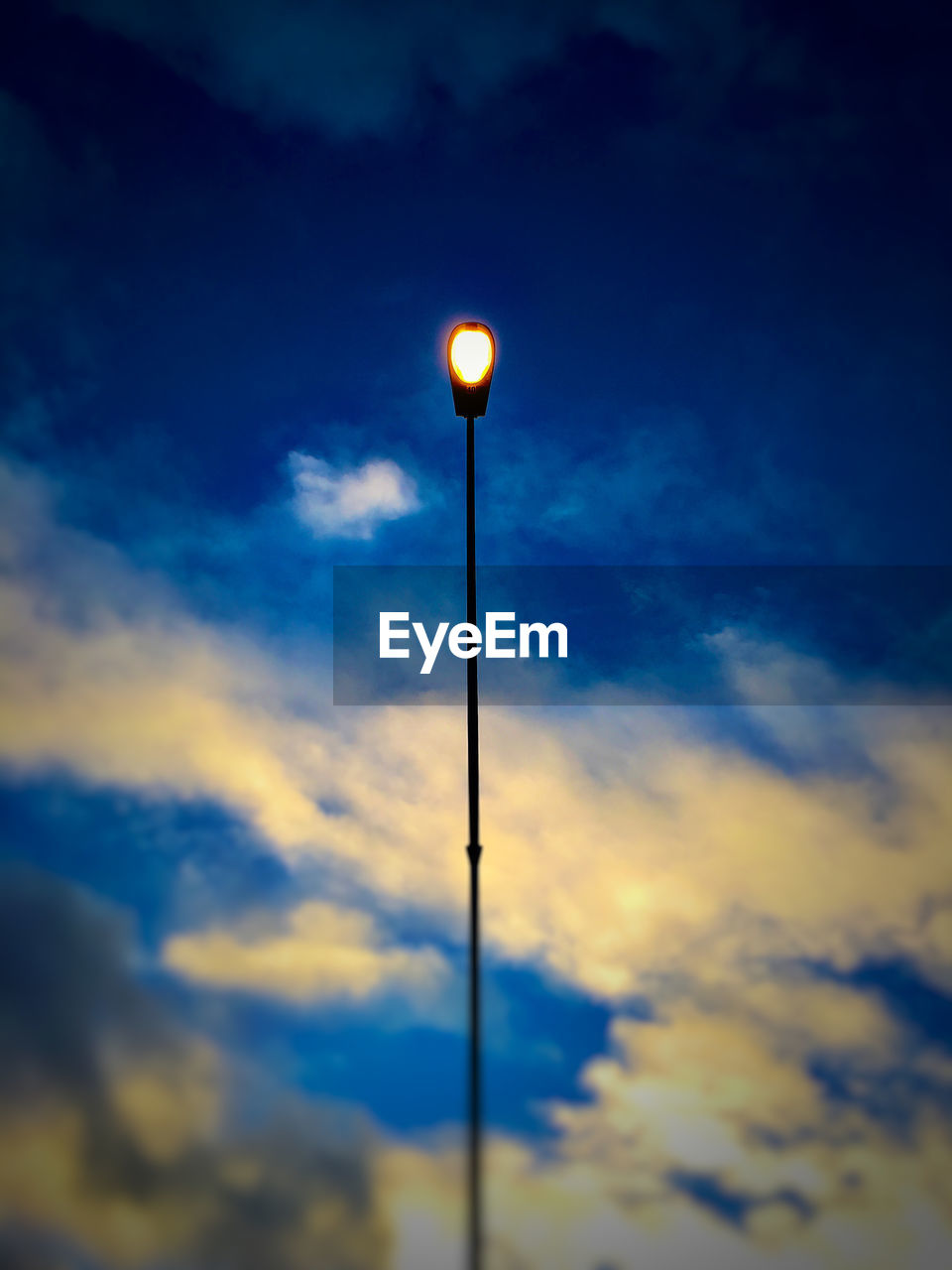 Low angle view of illuminated street light against cloudy sky