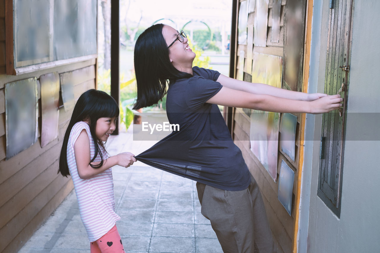 Side view of girl pulling mother locking window