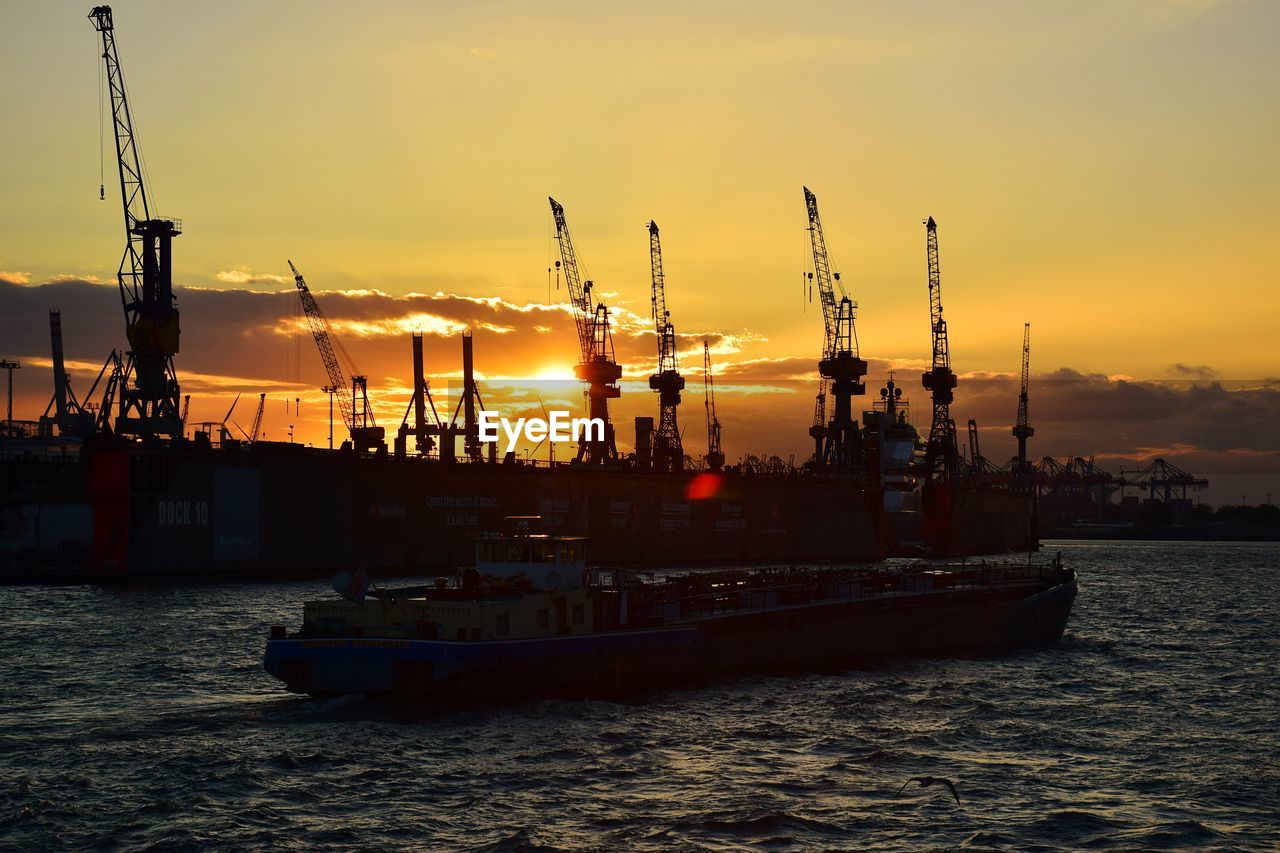 Boats in sea by commercial dock against sky during sunset