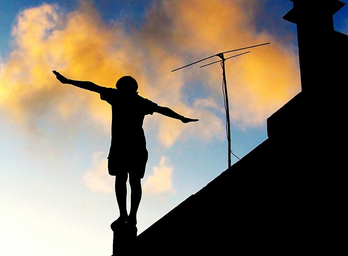 Low angle view of silhouette boy standing on roof during sunset