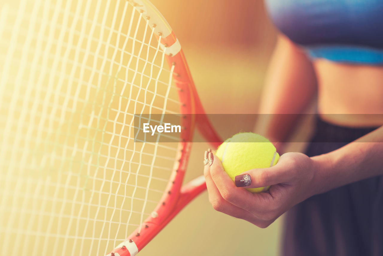 Midsection of woman holding tennis racket with ball while standing in court