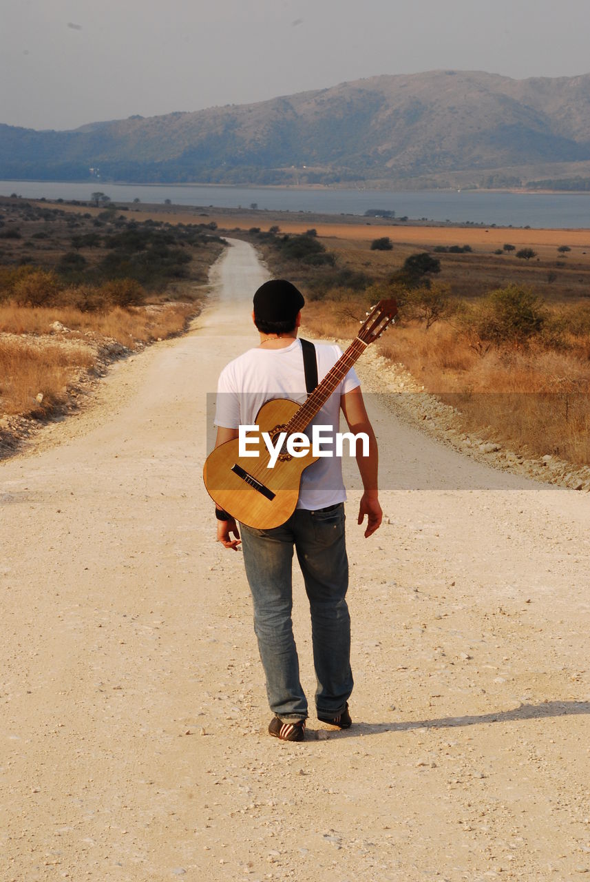 Rear view of man carrying guitar while walking on road