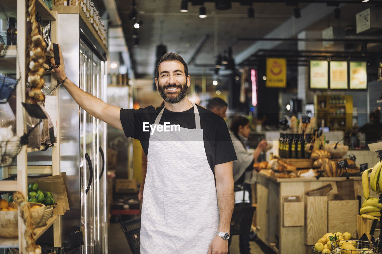 Portrait of smiling male retail clerk standing by rack at organic grocery store