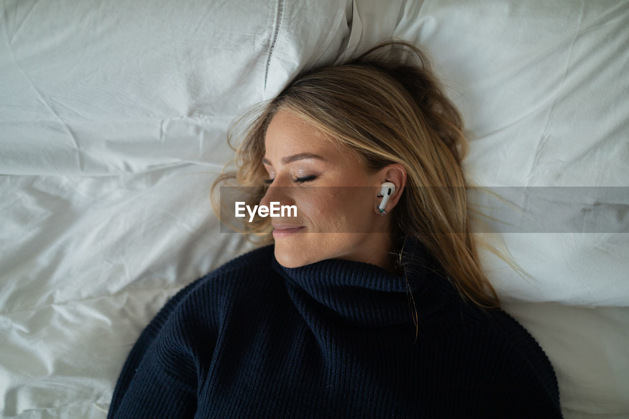 Woman listens to music with headphones in her bed in her apartment. mobile phone, technology.