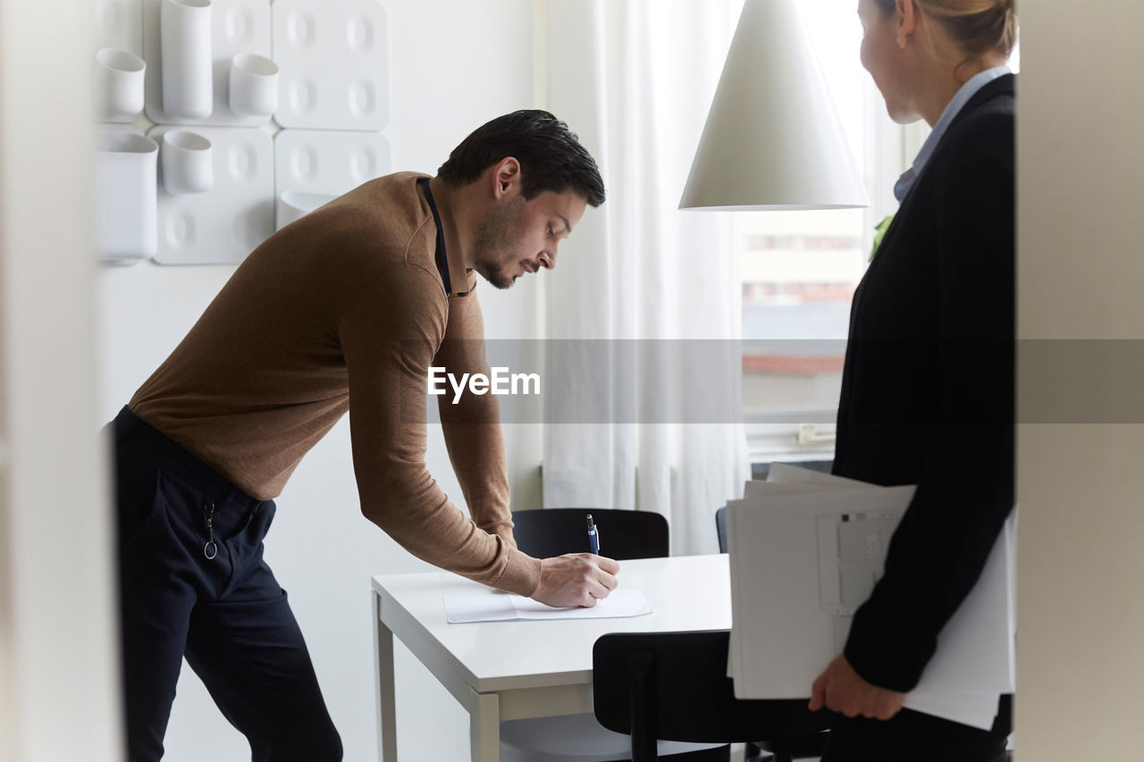 Mid adult man signing document while standing by real estate agent at new home