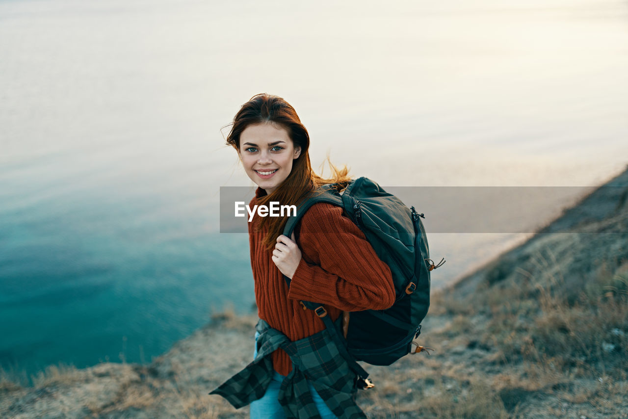PORTRAIT OF SMILING YOUNG WOMAN STANDING AGAINST WATERFALL