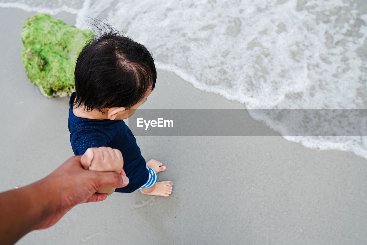 Cropped hand of father holding son hand while standing at beach