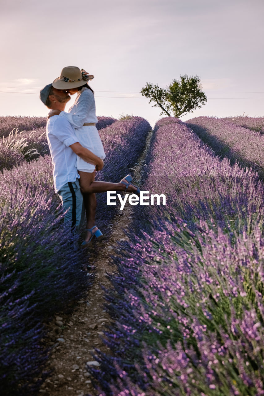 Side view of couple standing on flowering field against sky