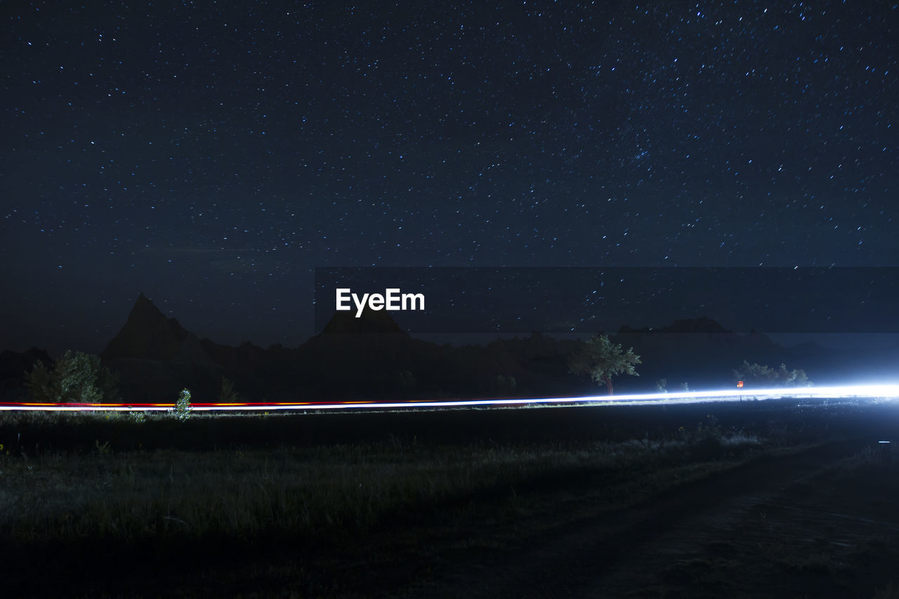 LIGHT TRAILS ON ROAD AGAINST STAR FIELD AT NIGHT