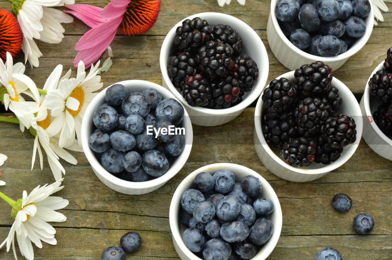 Blueberries and blackberries in small white ramekins with garden daisies on rustic wood table