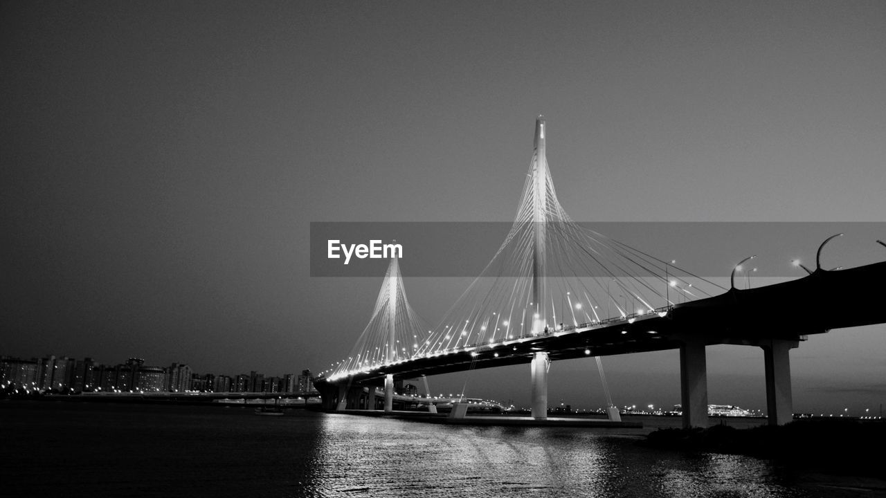 Bridge over river against sky in city at night