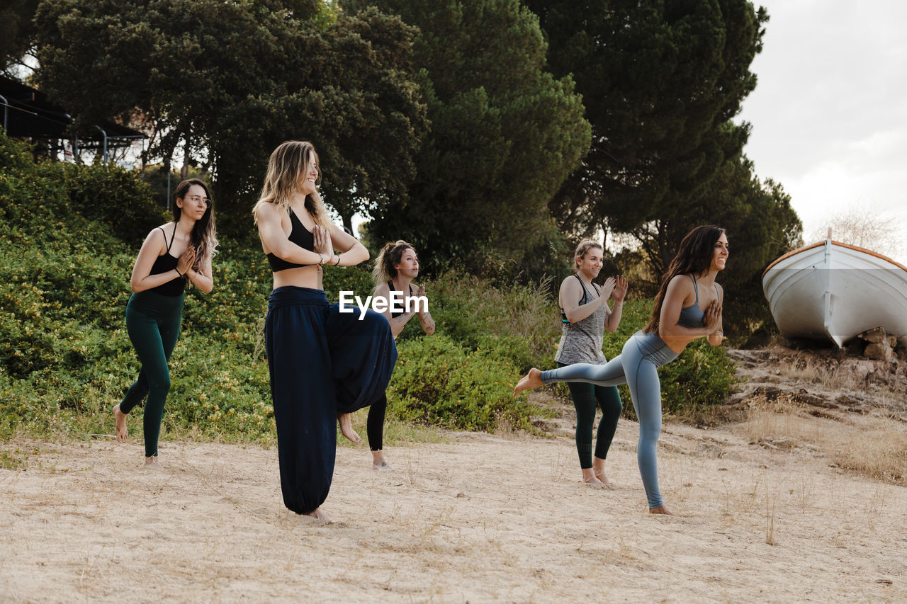 Smiling female instructor practicing yoga with friends against plants