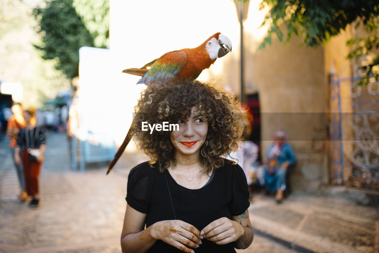 Smiling woman with macaw on head at street