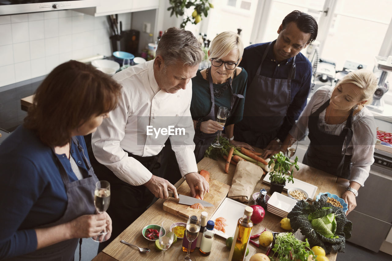 Concentrated students looking at chef cutting salmon in kitchen