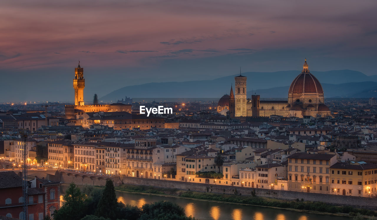 Illuminated buildings in city against sky during sunset