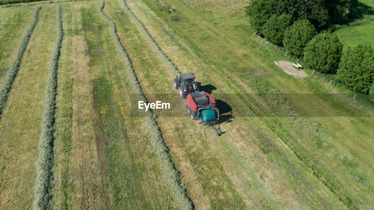 Black tractor with a red straw chamber press during the straw harvest on a mown field