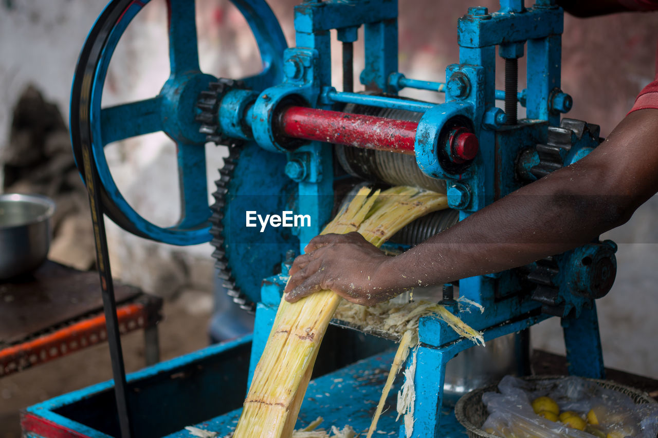 Cropped image of vendor holding sugar cane in machinery