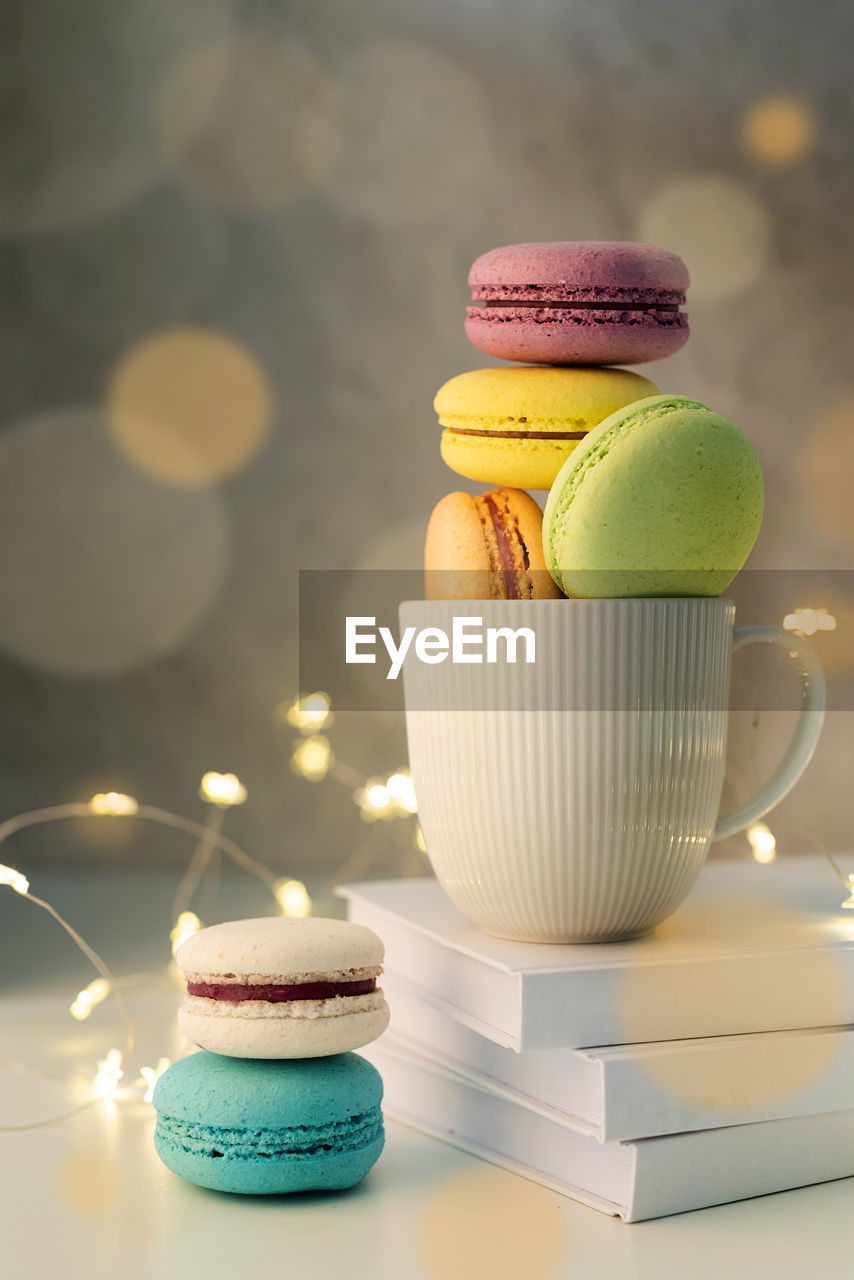 White coffee cup filled with macaroons on the table, fairy lights and bokeh background