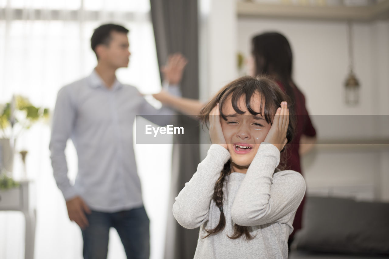 Close-up of girl crying while parents fighting in background at home