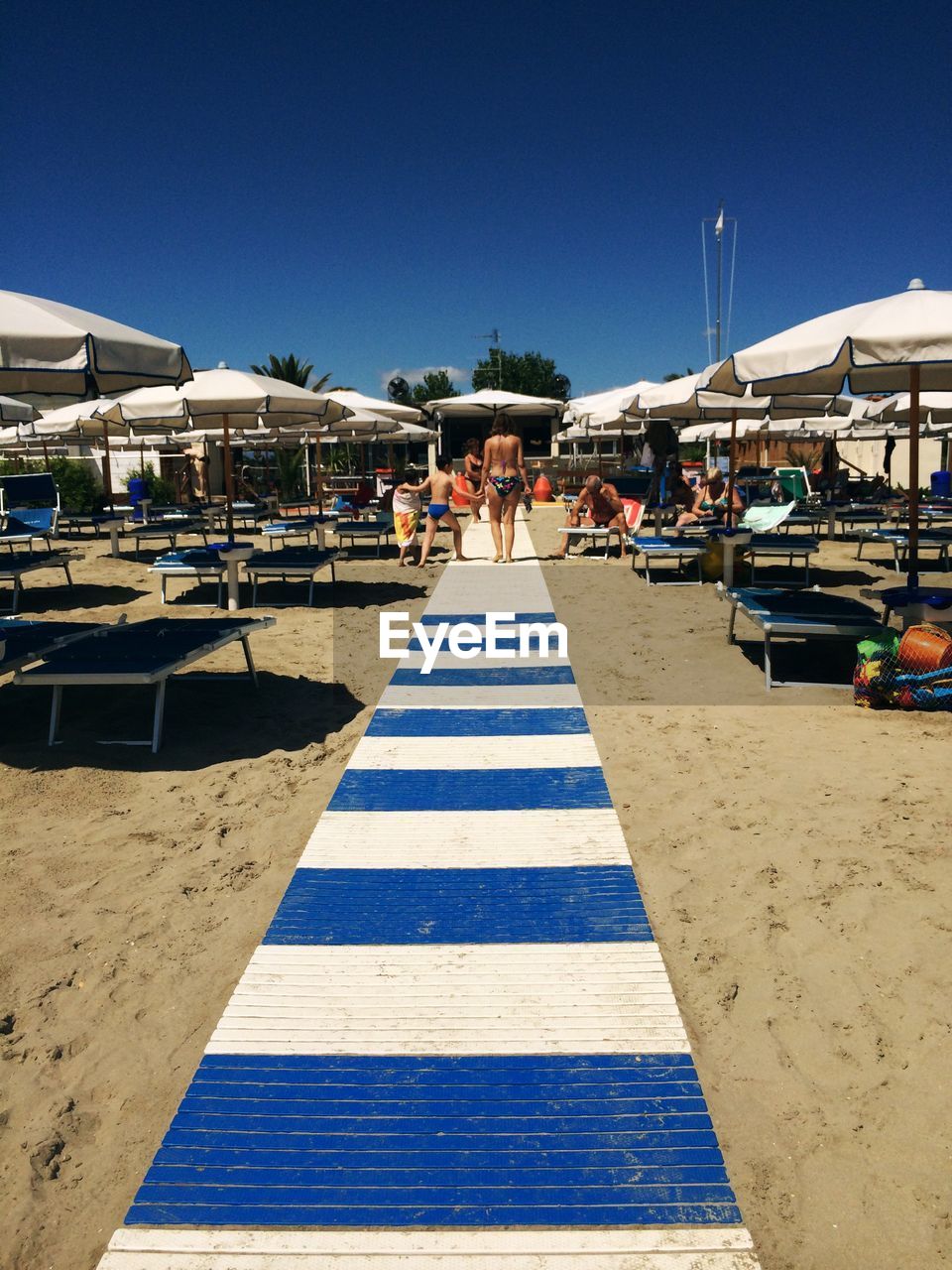 Footpath amidst parasols while people enjoying at beach against clear sky