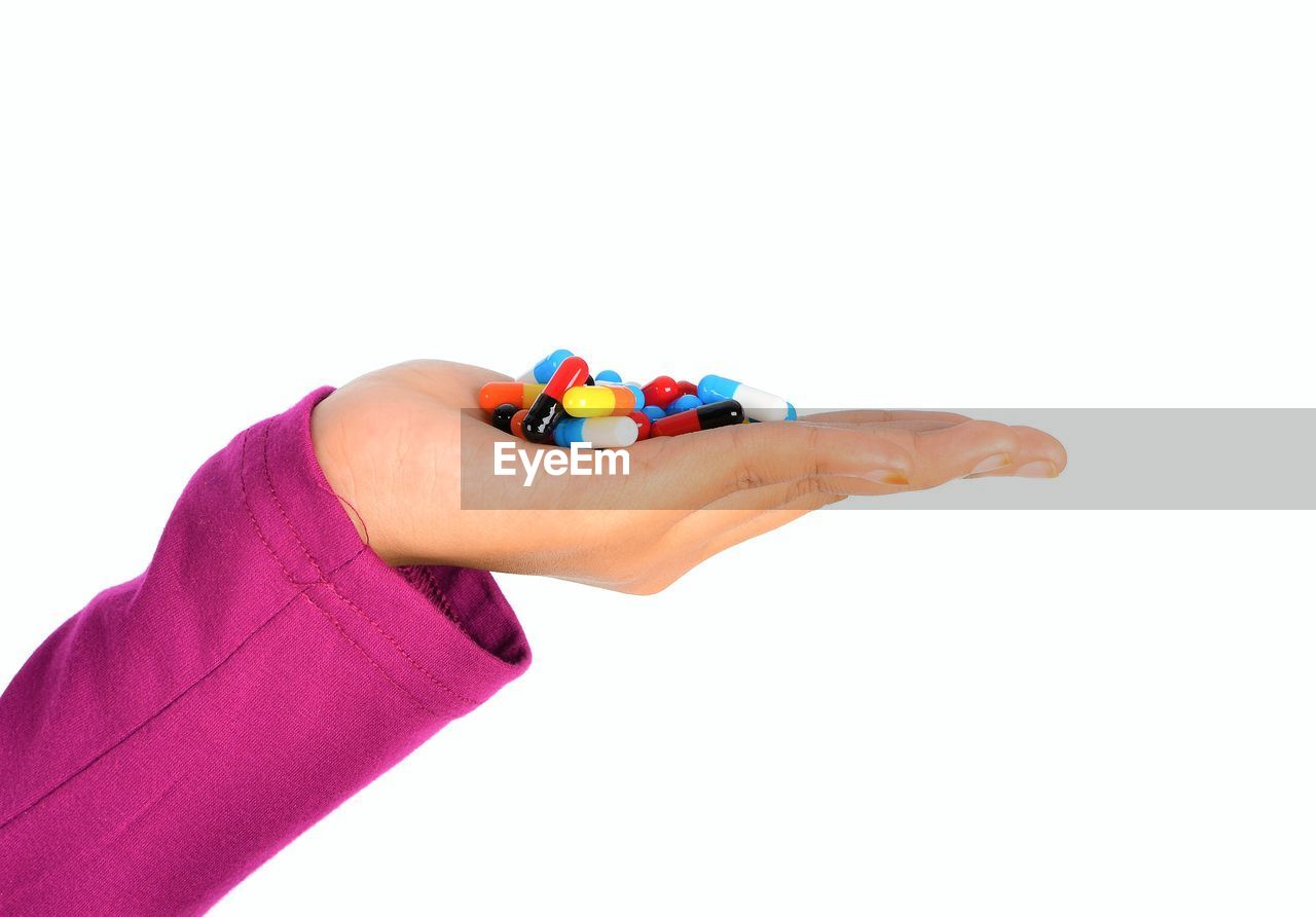 Cropped hand of doctor holding colorful capsules over white background