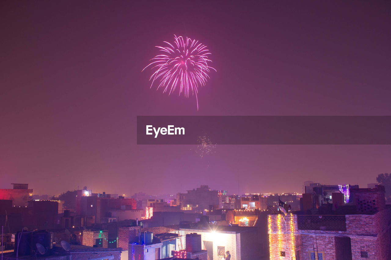 Low angle view of firework display over cityscape against sky at night