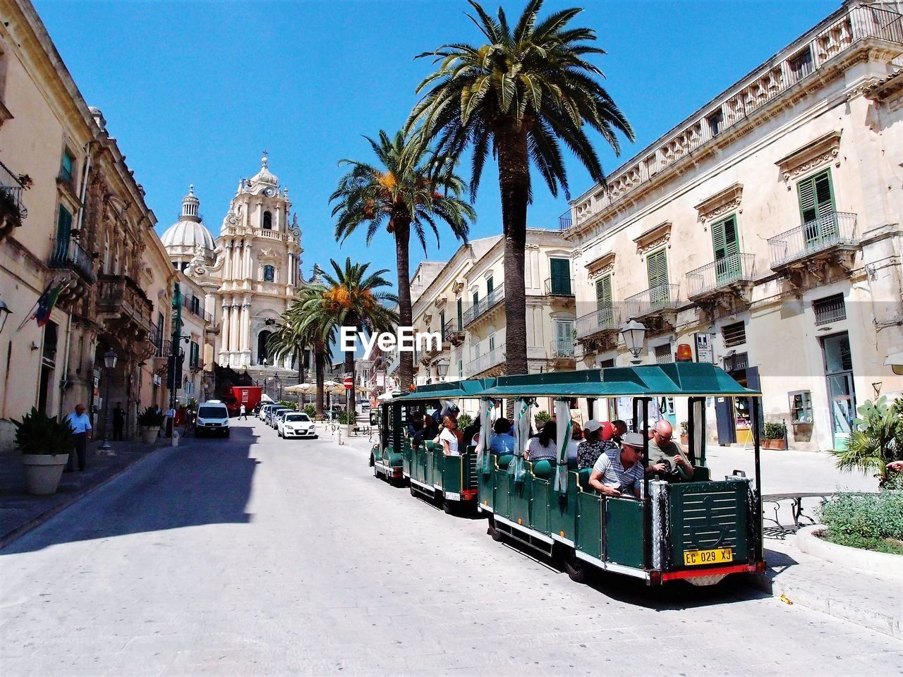 PEOPLE IN CITY STREET BY PALM TREES AND BUILDINGS IN FOREGROUND