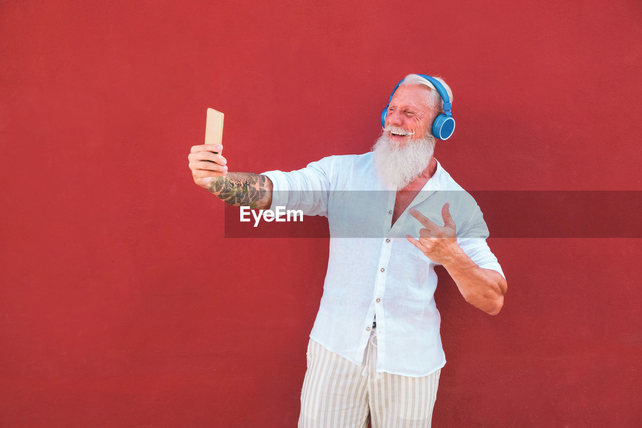 Cheerful man taking selfie with smart phone against red background