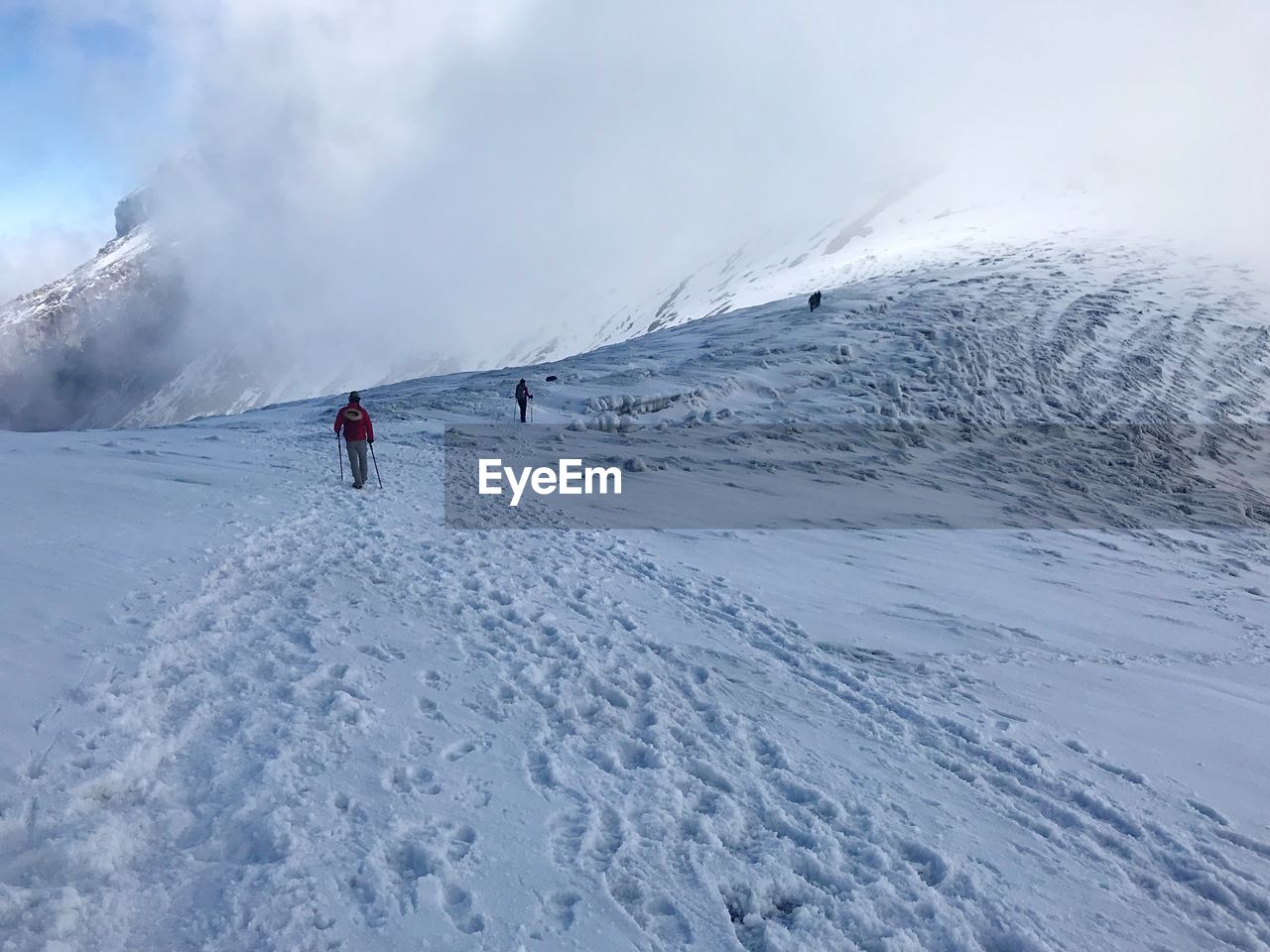 People on snow covered mountain against cloudy sky