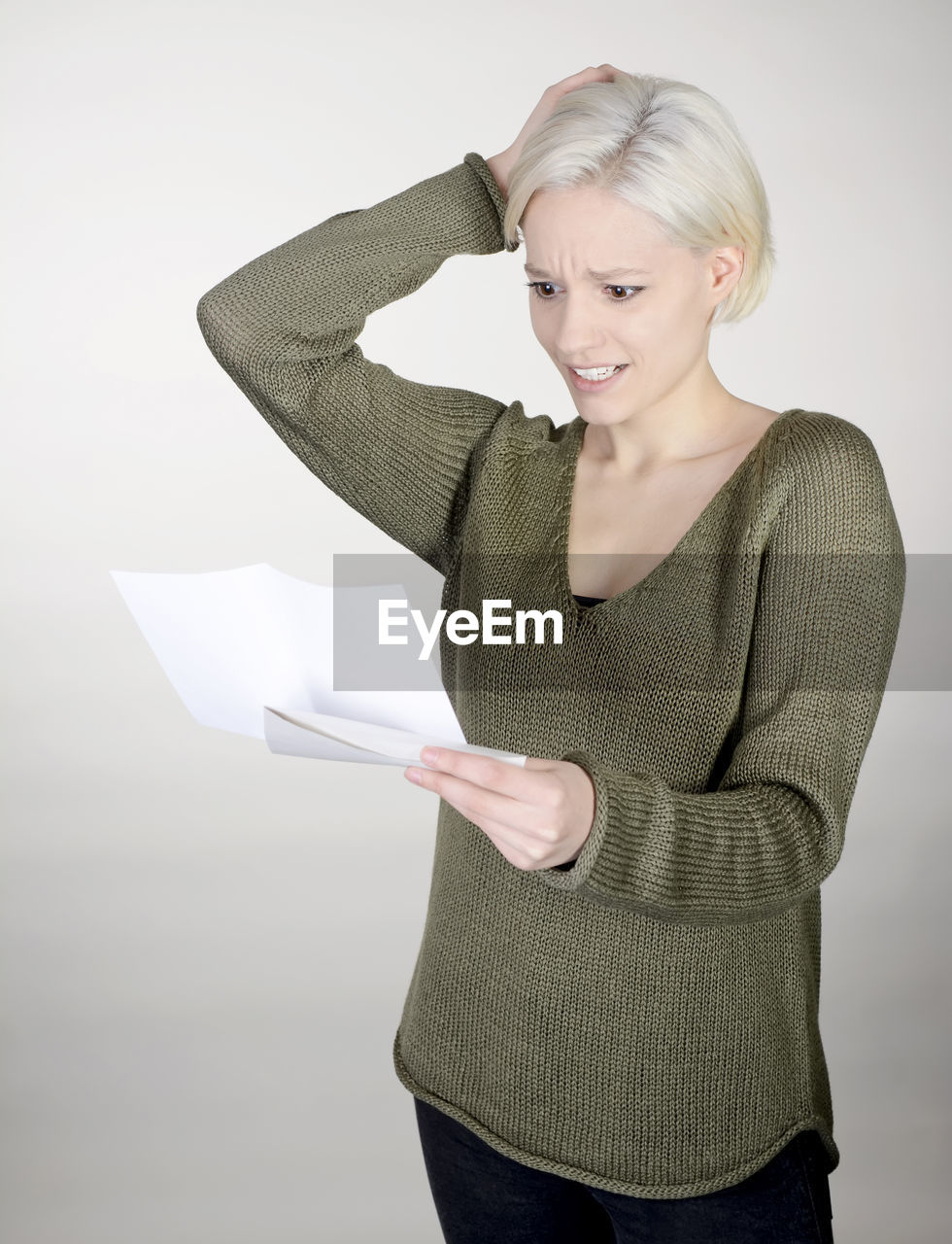 Shocked young woman reading paper while standing against white background