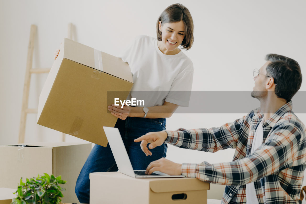 Man showing laptop to woman holding cardboard box