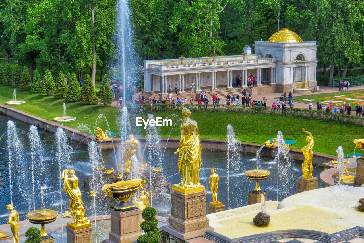 fountain, water, plant, architecture, water feature, nature, built structure, tree, group of people, large group of people, spraying, day, sculpture, travel destinations, crowd, building exterior, park, outdoors, pond, tourism, statue, garden, travel, park - man made space, formal garden, representation, town square, motion, splashing