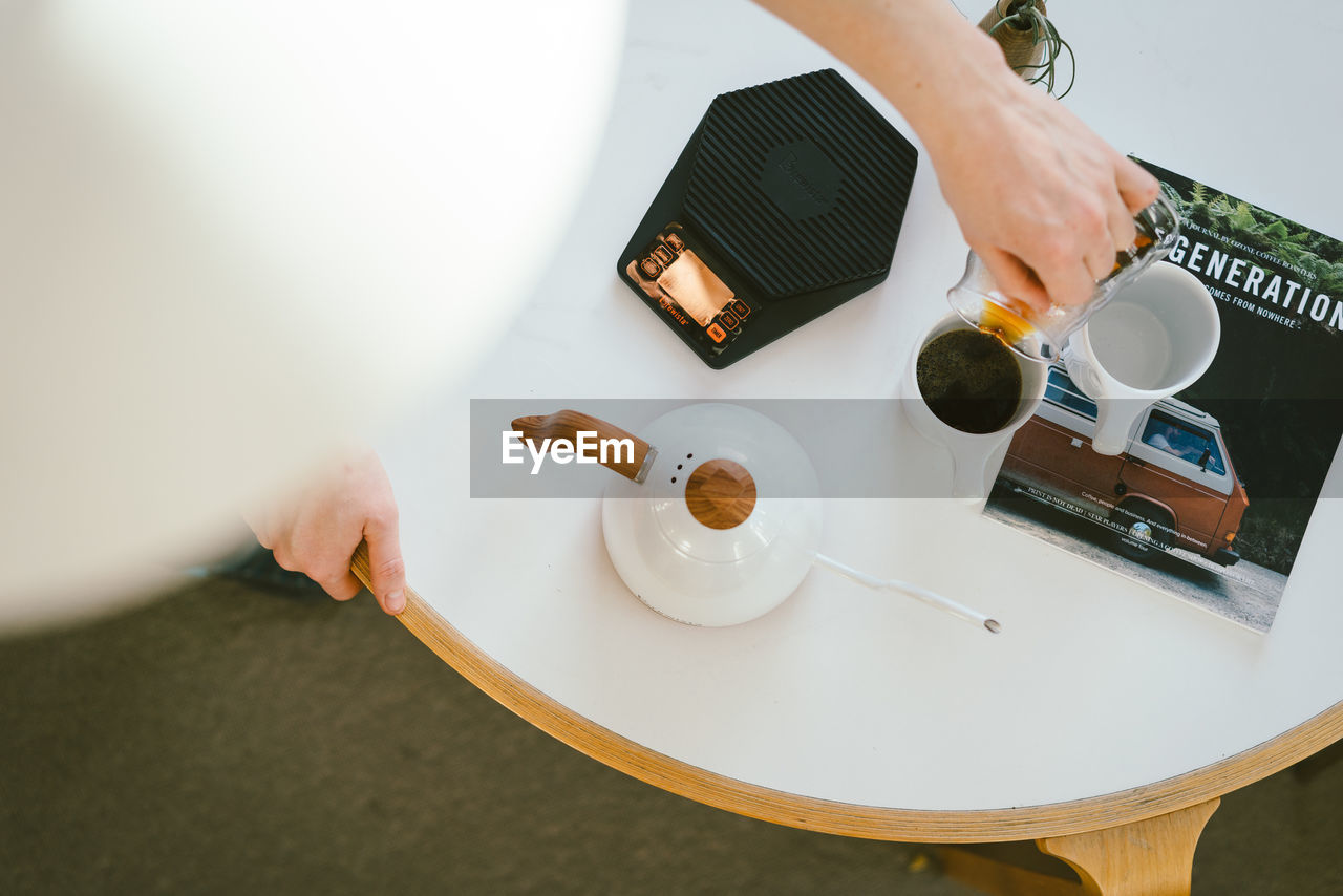 HIGH ANGLE VIEW OF HAND HOLDING COFFEE CUP AND TABLE