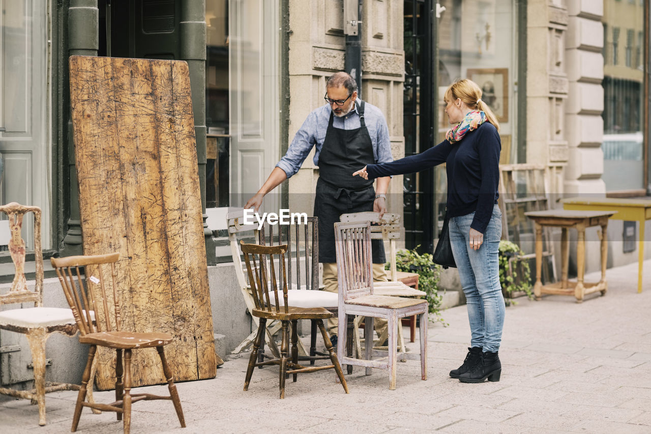 Female costumer pointing while retailer looking at chair outside antique shop