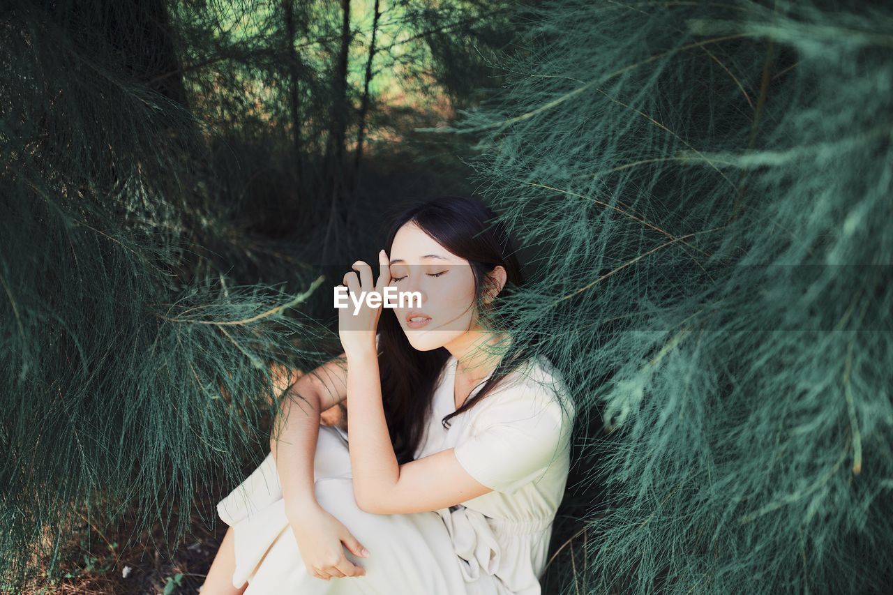 Young woman with eyes closed sitting by trees in forest