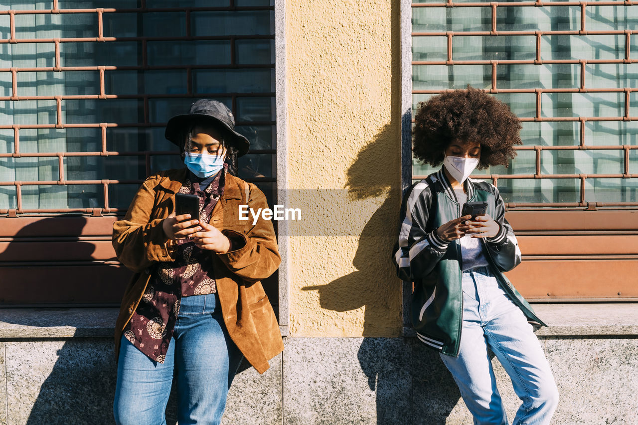 Multi-ethinc friends with protective face mask using smart phone on sunny day