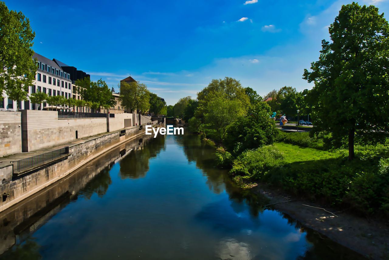 Canal amidst trees and buildings against sky