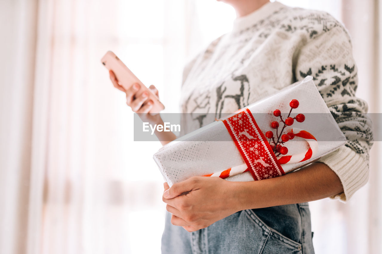 Midsection of man holding gift christmas box and watching mobile phone