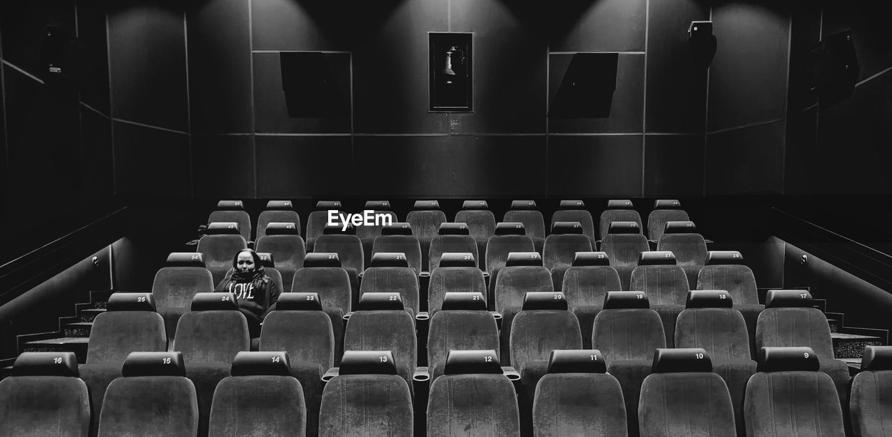 seat, auditorium, black and white, monochrome, in a row, indoors, movie theater, stage, arts culture and entertainment, theatre, chair, monochrome photography, no people, empty, stage theater, black, repetition, absence, large group of objects, side by side