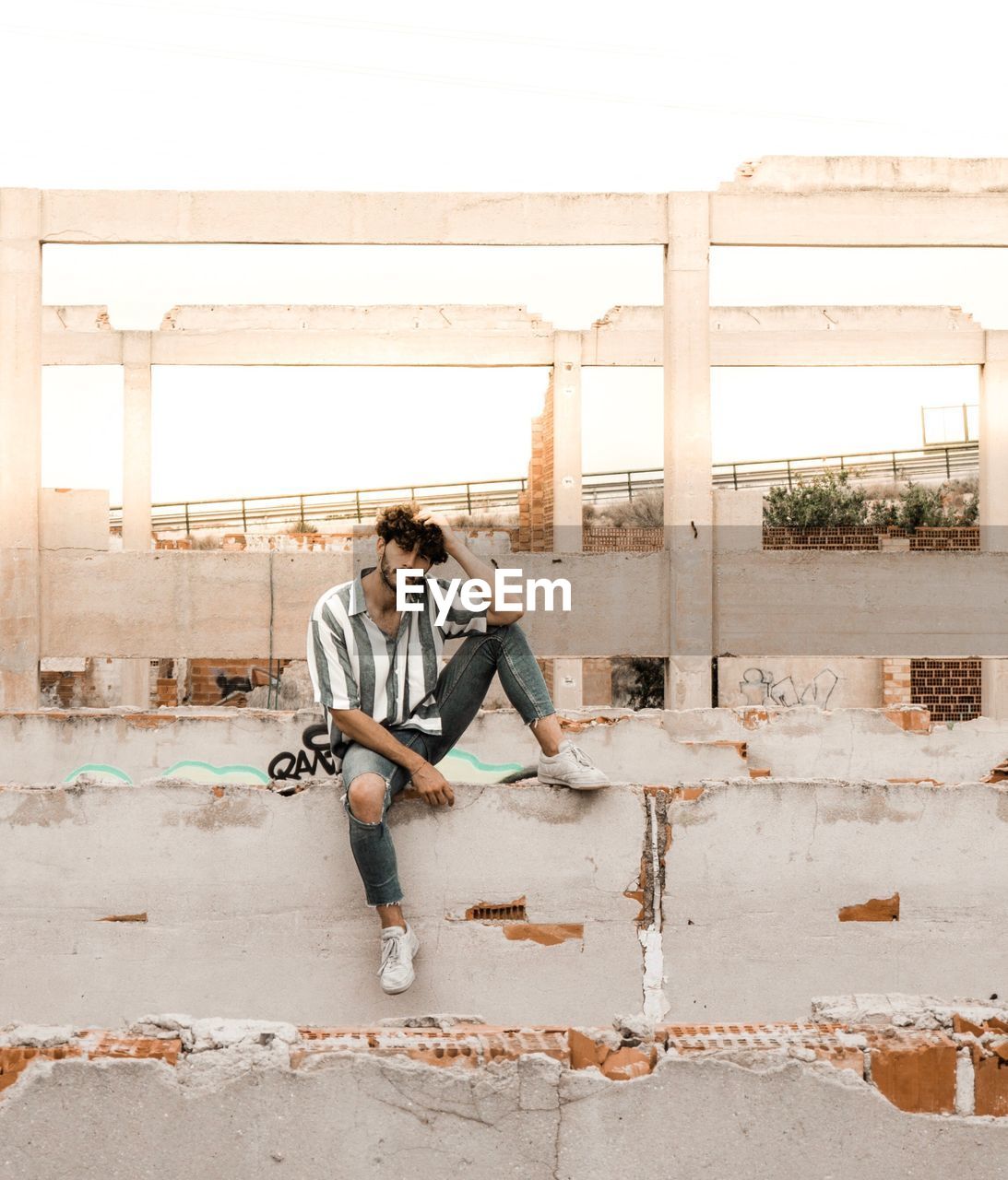 Full length of young man sitting on retaining wall in old ruins