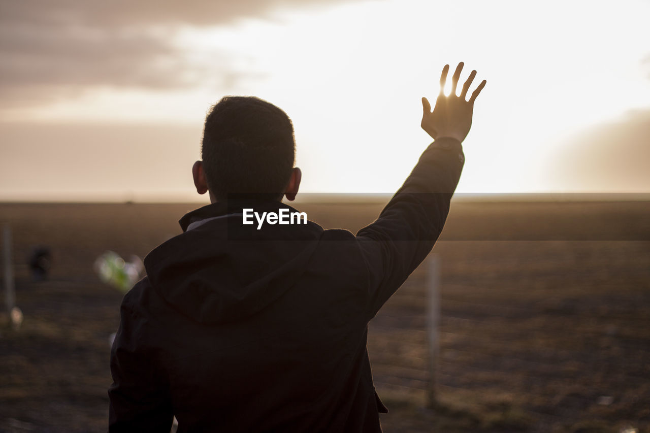 Rear view of man standing by sea against sky during sunset