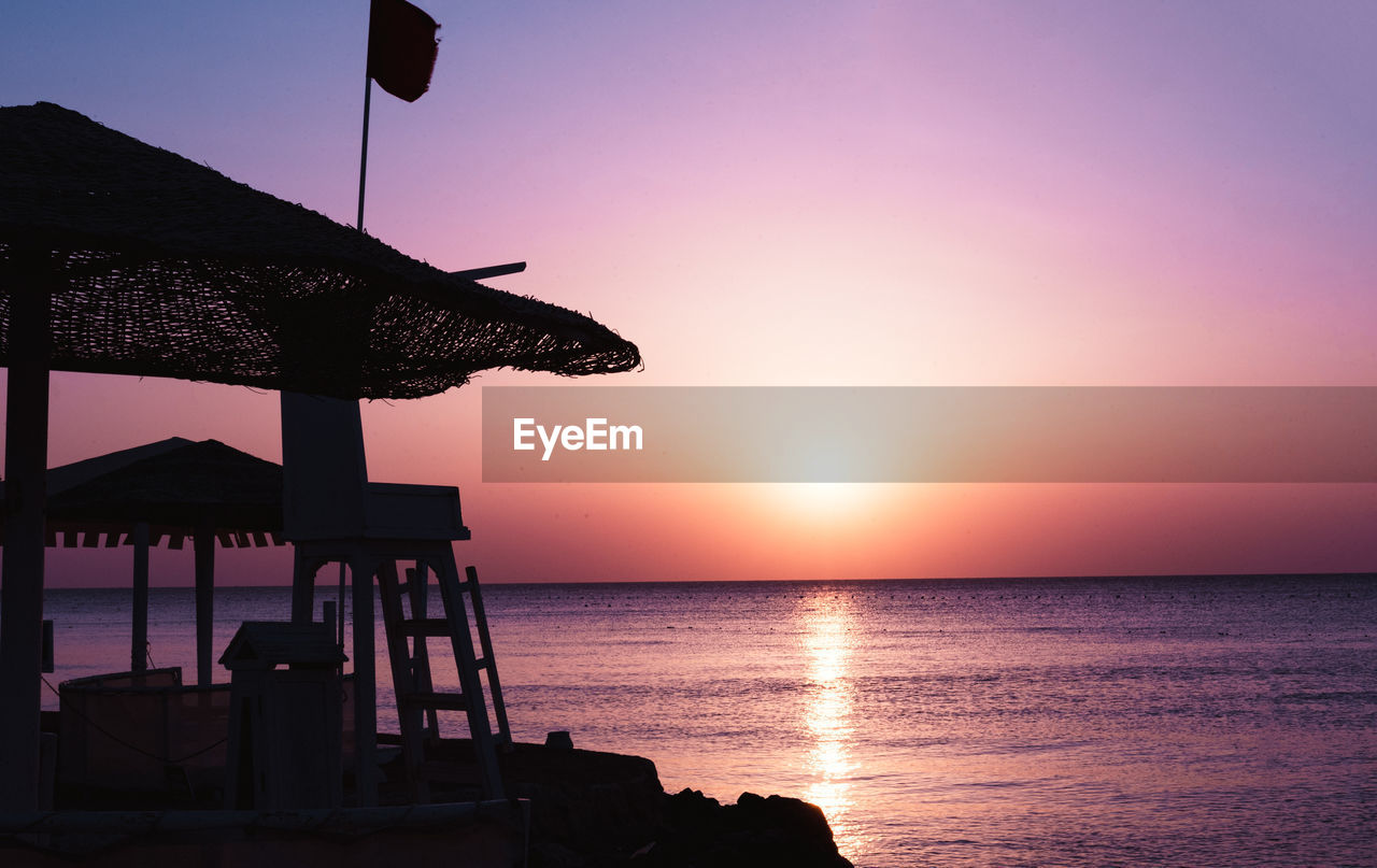 sea, water, sky, sunset, beach, ocean, horizon over water, horizon, dusk, land, nature, beauty in nature, silhouette, evening, architecture, tranquility, scenics - nature, sun, tranquil scene, built structure, hut, coast, travel destinations, idyllic, no people, outdoors, lifeguard hut, vacation, travel, seascape, trip, sunlight, holiday, clear sky, man made structure, summer, shore
