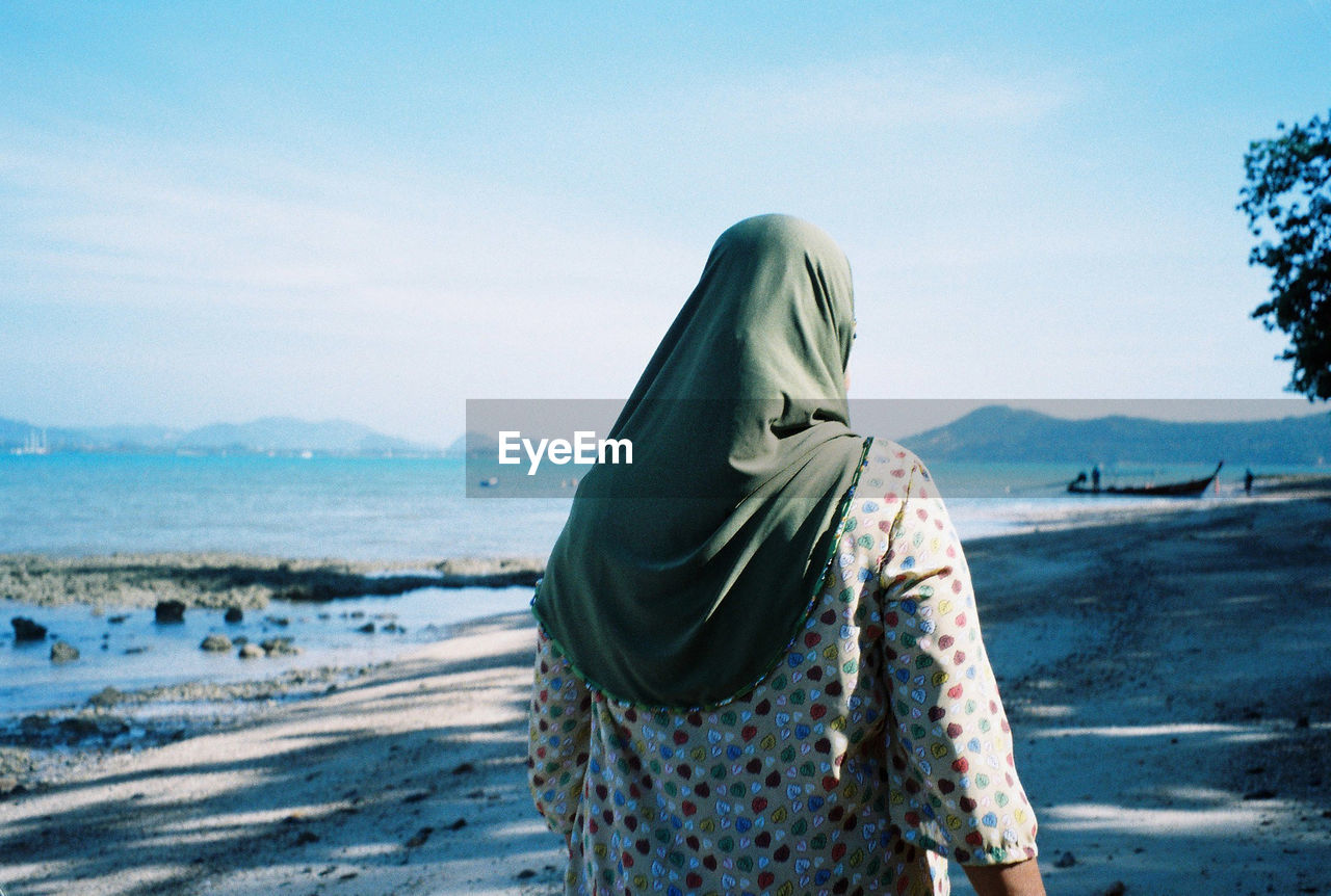 Rear view of woman wearing hijab walking at beach against sky