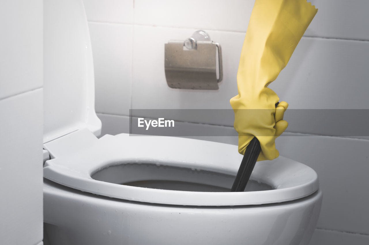 Cropped hand of person wearing yellow protective glove while washing toilet bowl