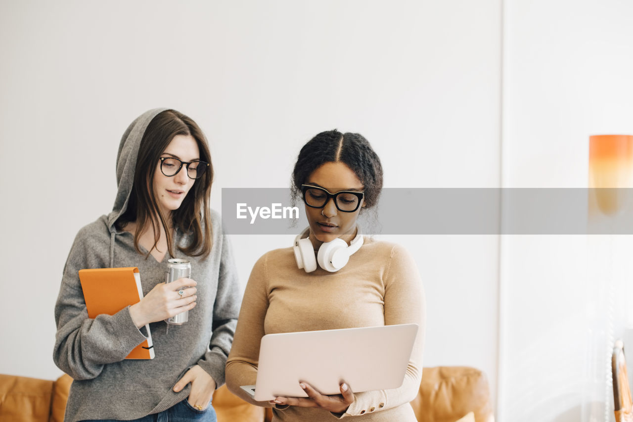 Female computer programmers discussing over laptop while standing in office