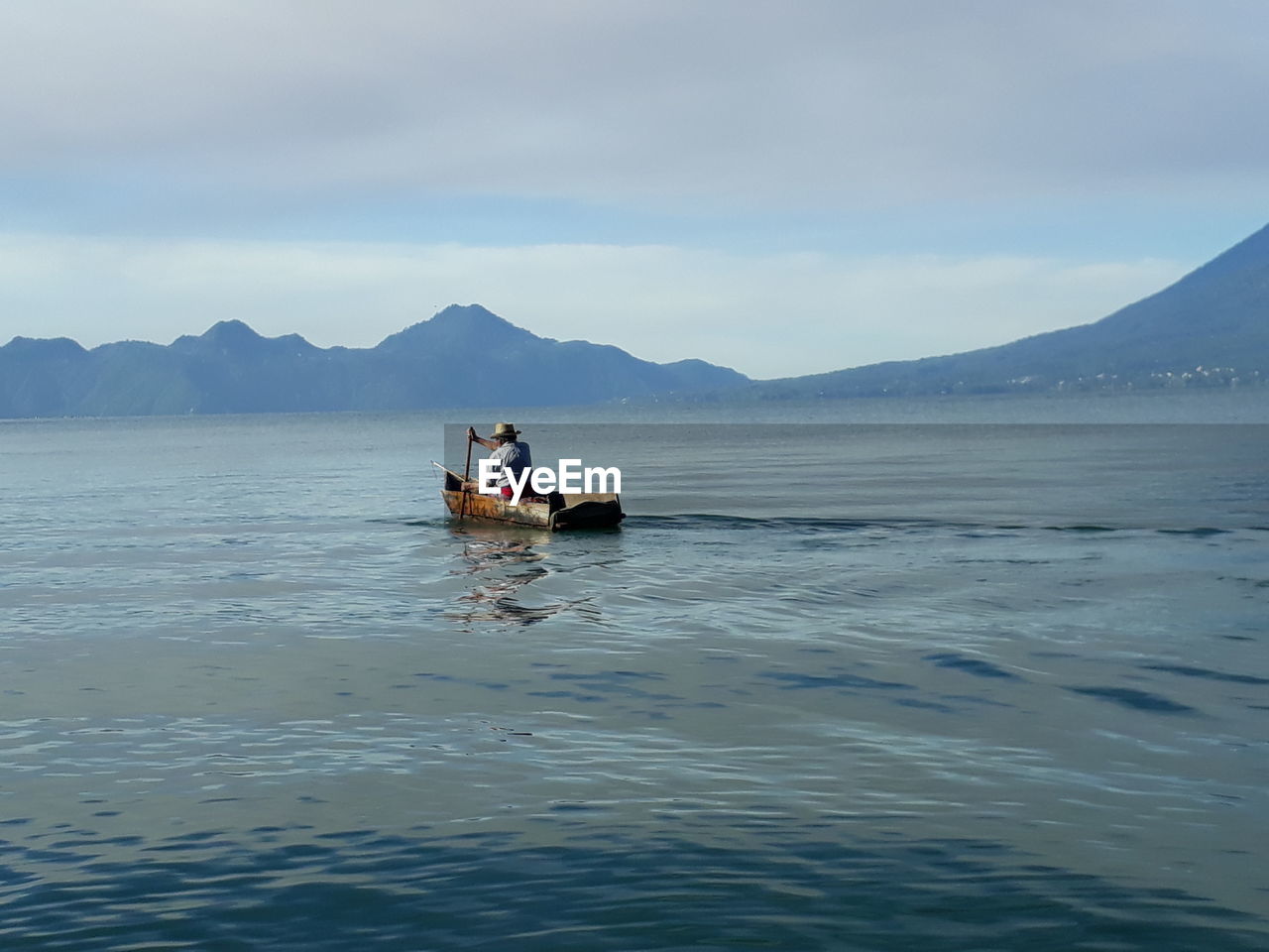 Rear view of man boating in lake against sky