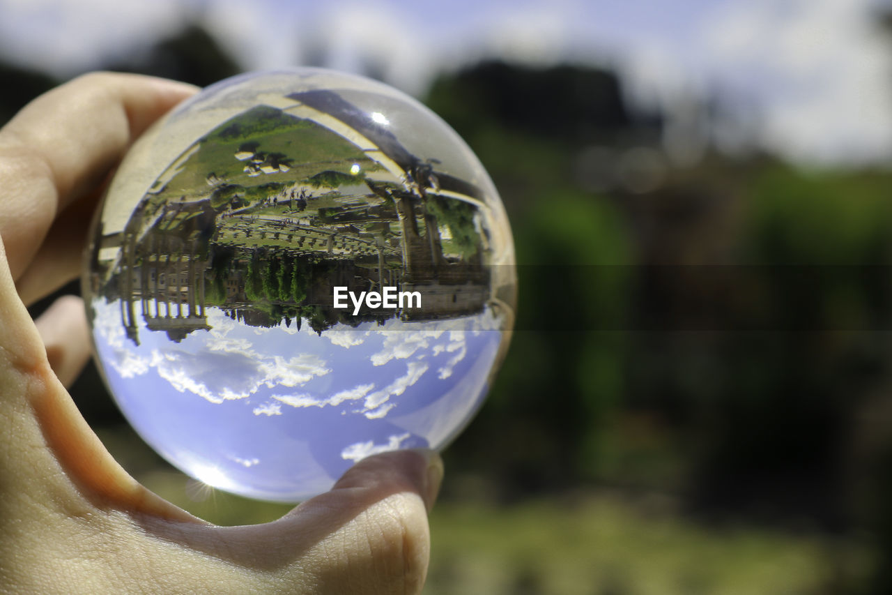 CLOSE-UP OF HAND HOLDING CRYSTAL BALL WITH REFLECTION OF PERSON