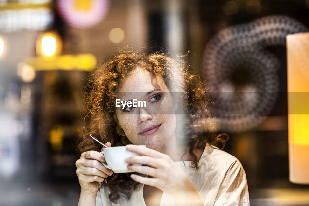 Portrait of smiling young woman with coffee cup behind windowpane of a coffee shop